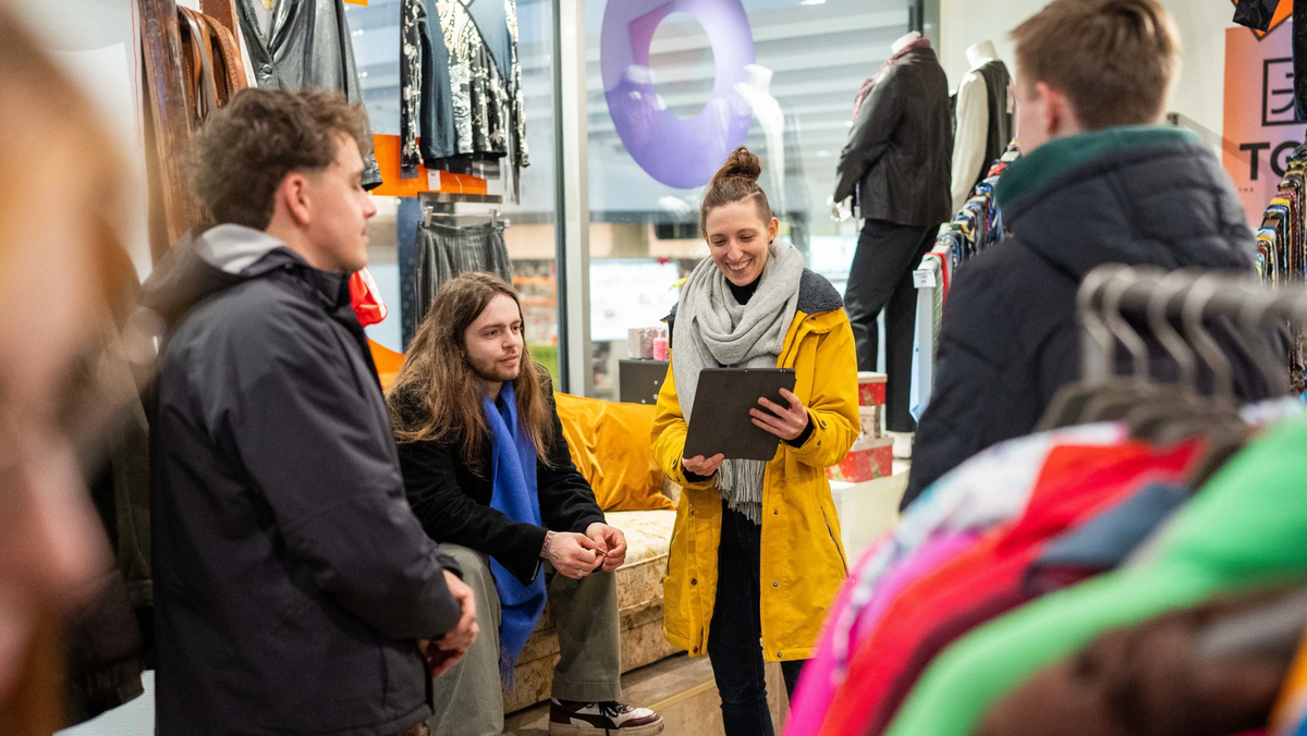 In einem Second Hand Modeladen in Stuttgart erläutert unser Guide Sabrina einer kleiner Gruppe die Vorteile von nachhaltiger Mode.