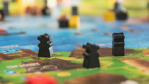 Spielfiguren auf einem Spielbrett mit Wasser- und Landflächen im Hintergrund