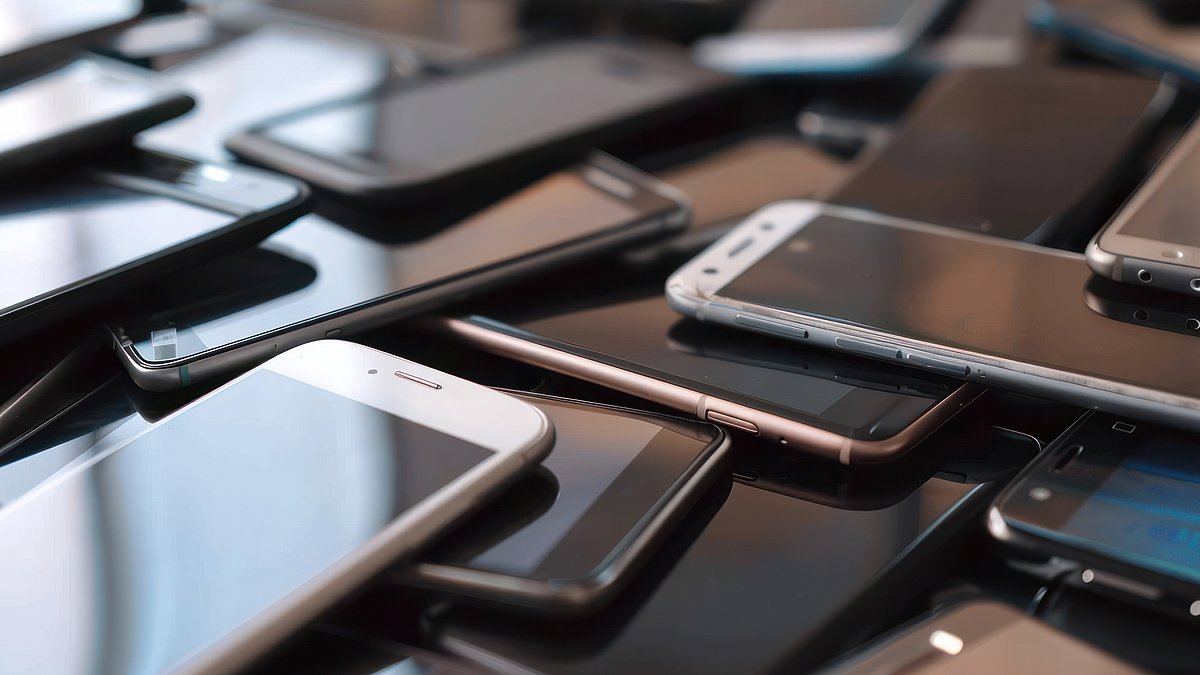 Fair telefonieren Viele Handys liegen aufeinander gestapelt auf einem Tisch.