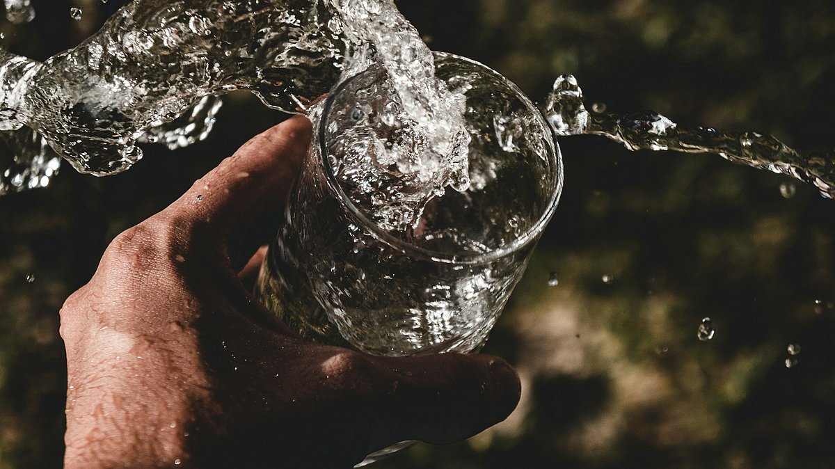 Wasser wird aus einem Glas verschüttet, das von einer Hand gehalten wird.
