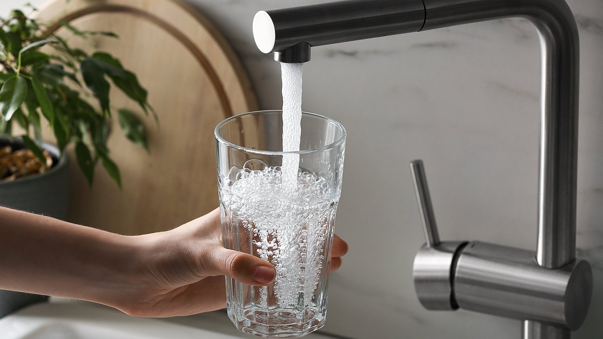 Eine Person hält ein Glas unter den laufenden Wasserhahn.