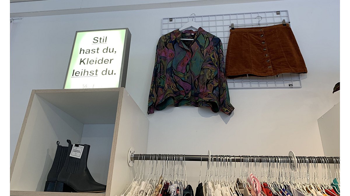 In der Kleiderei steht auf einem Regal eine Leuchtreklame mit dem Text: Stil hast du, Kleider leihst du.