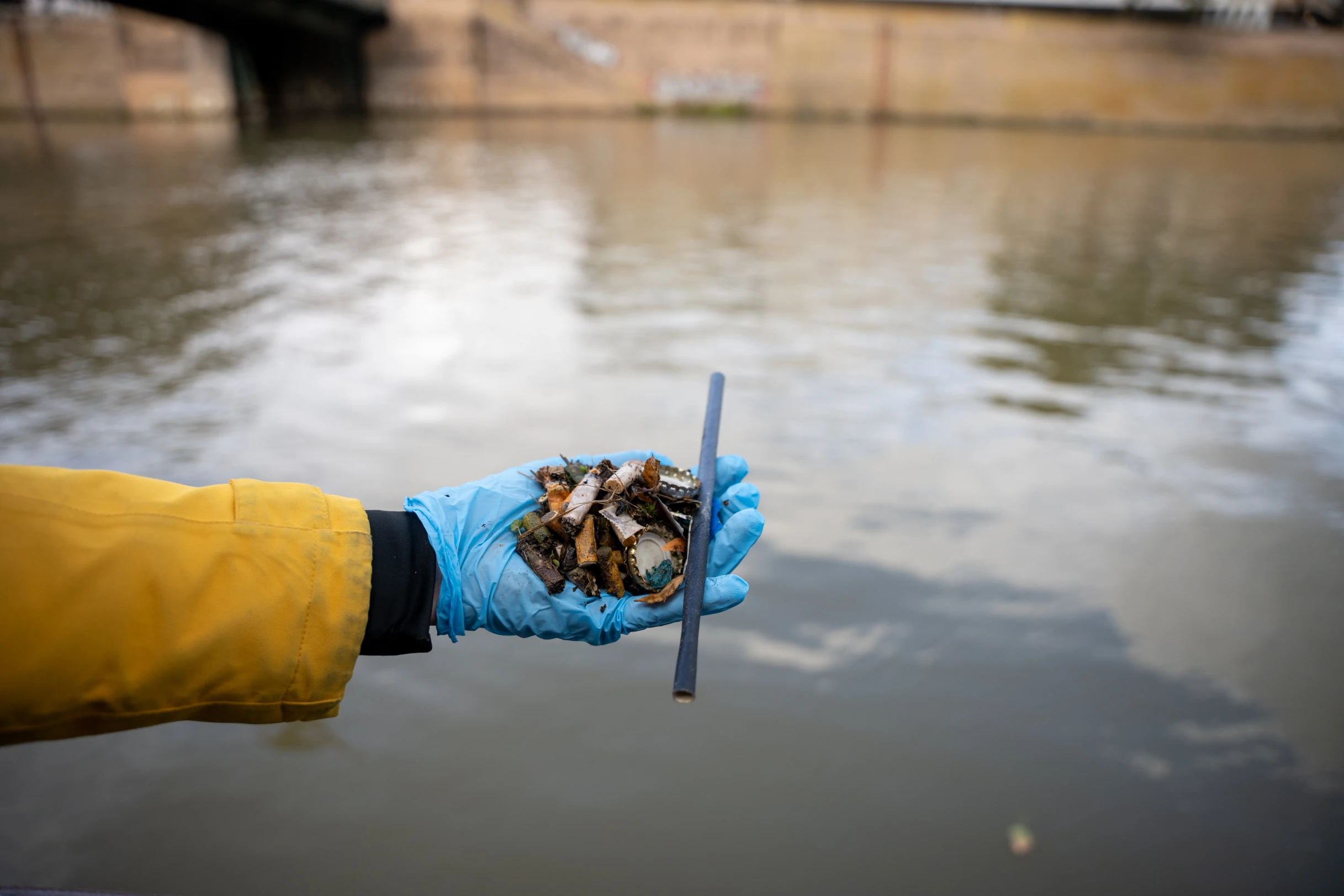 Eine Hand, die Müll aus einem Fluss sammelt.